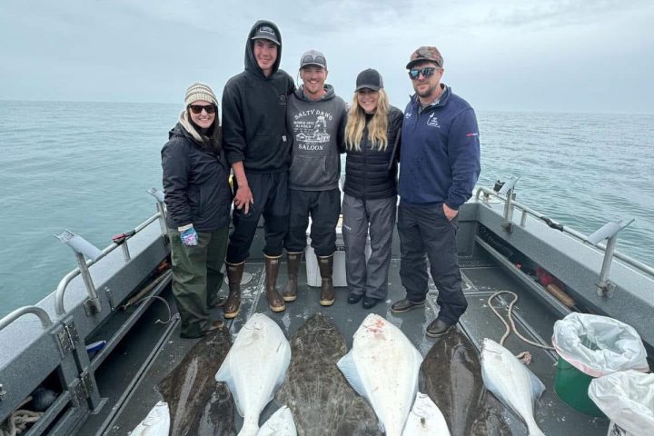 Five people on a boat with large fish laid out on the deck.