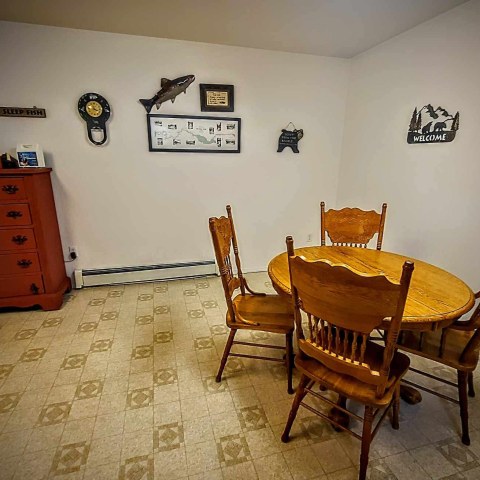 Dining area with a round wooden table, four chairs, red dresser, and wall decorations.