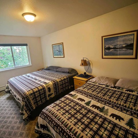 Bedroom with two beds, patterned quilts, window, and framed picture on wall.