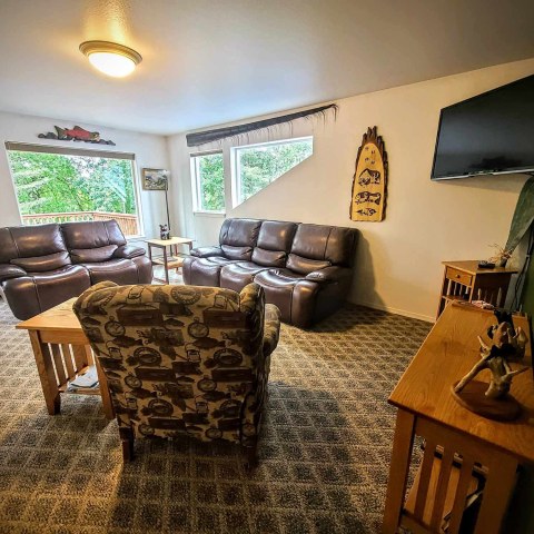 Cozy living room with leather sofas, patterned armchair, TV, and large windows with garden view.