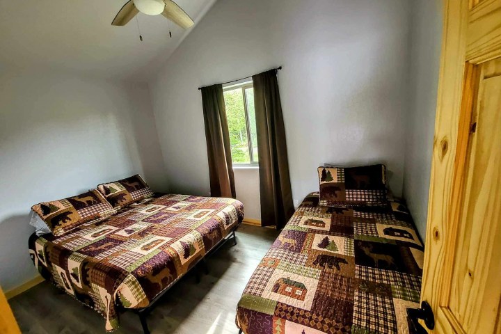 Room with two beds, wooden door, window with curtains, and quilted bedding with forest theme.