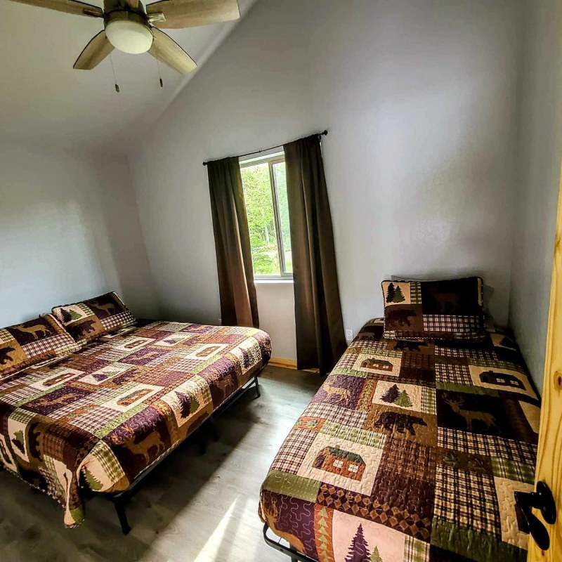 Room with two beds, wooden door, window with curtains, and quilted bedding with forest theme.