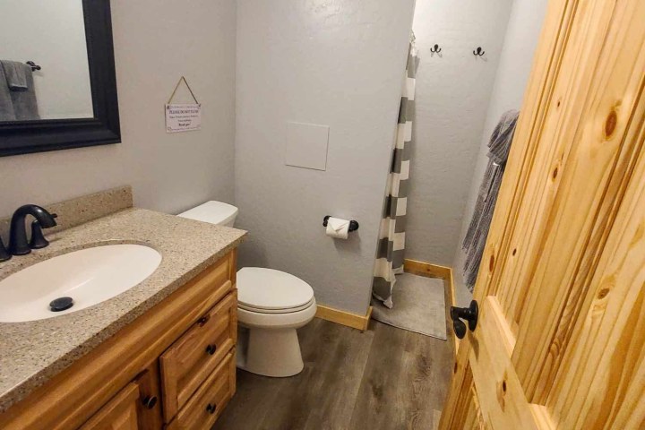 Bathroom with wooden vanity, toilet, and shower with striped curtain.