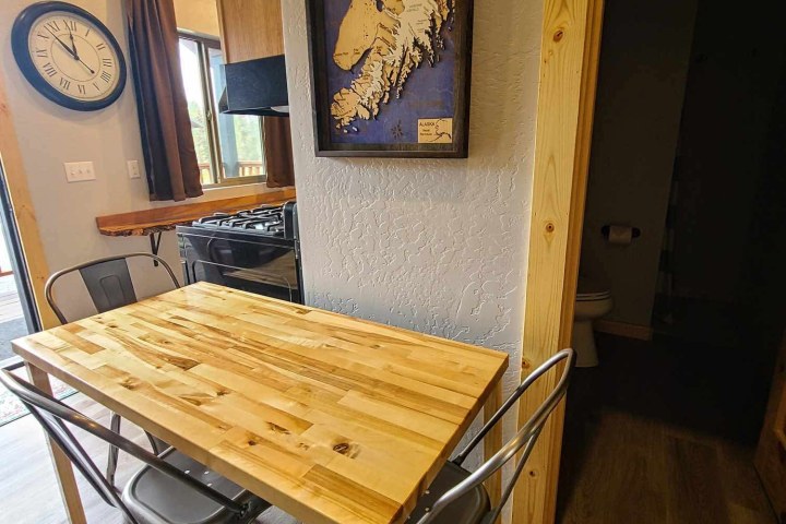 Small dining area with wooden table, metal chairs, wall clock, and framed map.