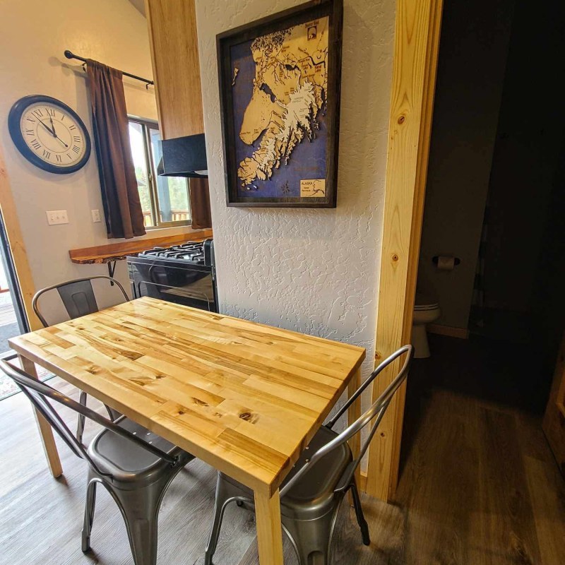 Small dining area with wooden table, metal chairs, wall clock, and framed map.