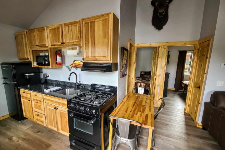 Rustic kitchen with wood cabinets, black appliances, and antelope head wall mount above.