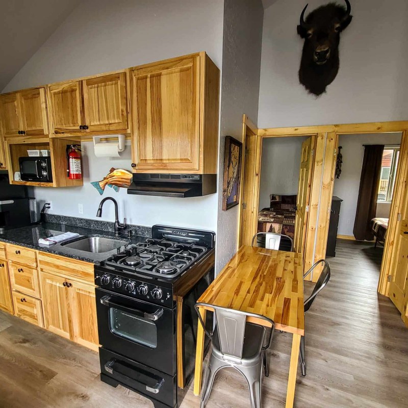 Rustic kitchen with wood cabinets, black appliances, and antelope head wall mount above.