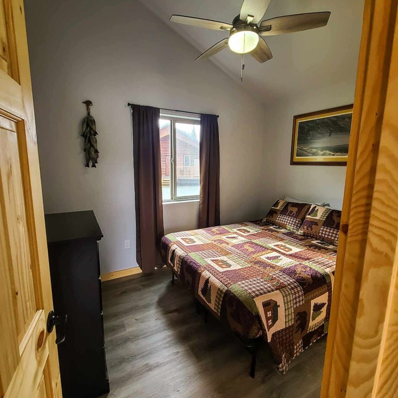 Cozy bedroom with quilt, ceiling fan, artwork, and window with curtains.