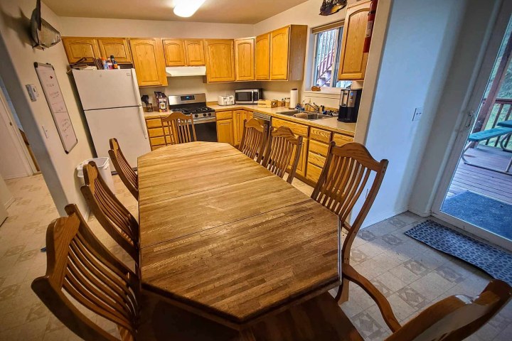 Kitchen with wooden table, eight chairs, oak cabinets, white fridge, and stove under bright ceiling light.