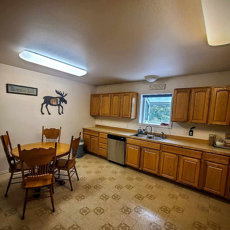 Kitchen with wooden cabinets, round table, chairs, wall decorations, and natural light from a window.